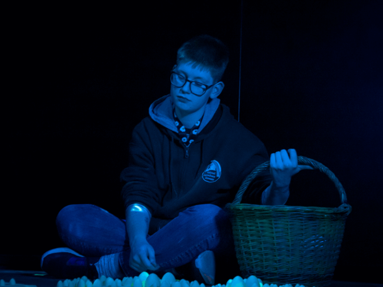 Boy in blue-lit folklore scene at the National Leprechaun Museum sitting with a wicker basket among glowing fairy-themed props.