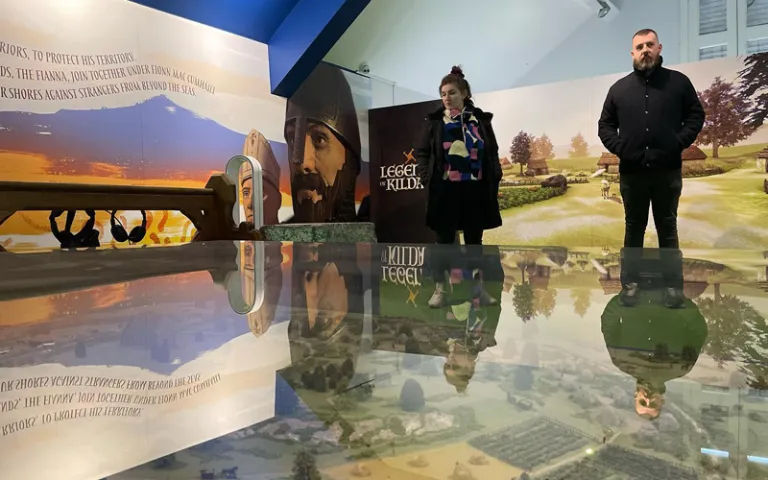 Visitors exploring the Legends of Kildare exhibit, featuring Irish myth-inspired murals and a reflective model landscape.