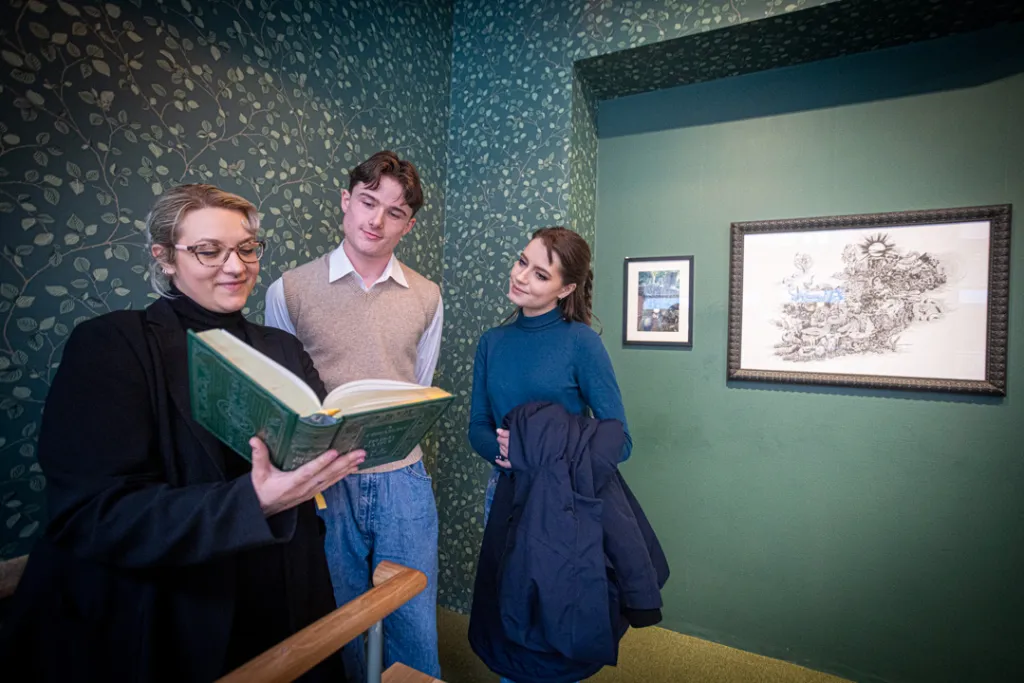 Woman showing an illustrated folklore book to a young man and woman, inside a green patterned storytelling room at the National Leprechaun Museum.