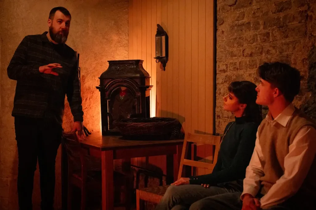 Storyteller shares Irish folklore inside the National Leprechaun Museum’s cottage room as visitors listen beside a glowing hearth and traditional props.