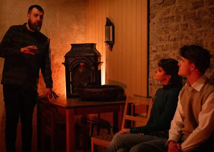Storyteller shares Irish folklore inside the National Leprechaun Museum’s cottage room as visitors listen beside a glowing hearth and traditional props.
