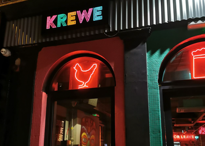 Colourful neon-lit exterior of Krewe restaurant in Dublin, featuring vibrant signage and glowing chicken icon.