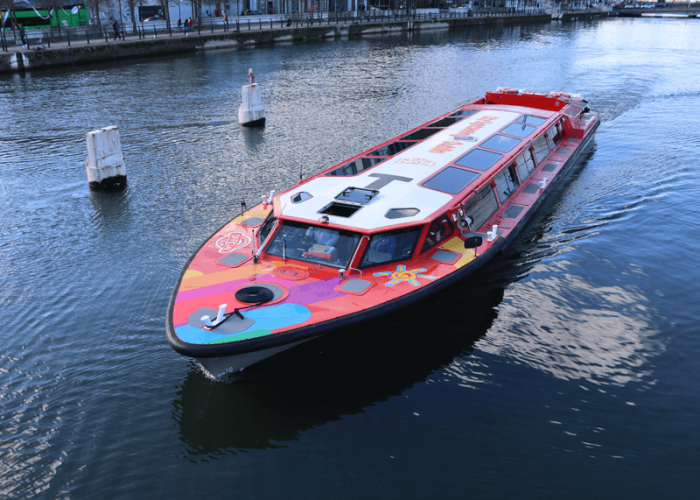 Colourful tour boat cruising along the River Liffey in Dublin on a bright day.