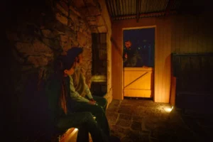 Visitors listening to a guide speaking through a half-door in a softly lit stone cottage room during a storytelling moment at the National Leprechaun Museum.