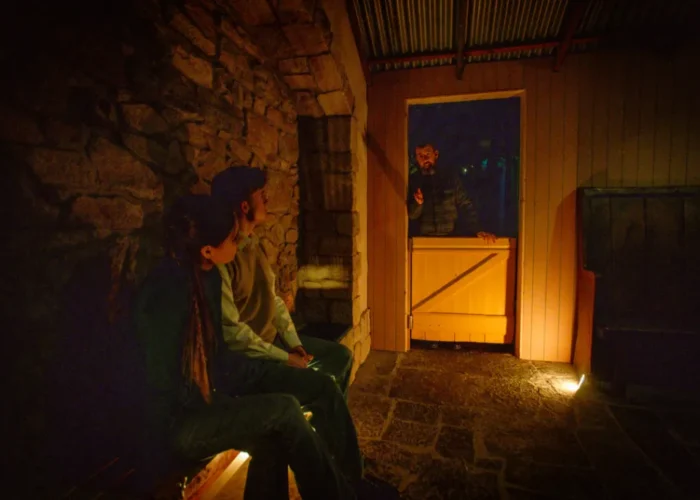 Visitors listening to a guide speaking through a half-door in a softly lit stone cottage room during a storytelling moment at the National Leprechaun Museum.
