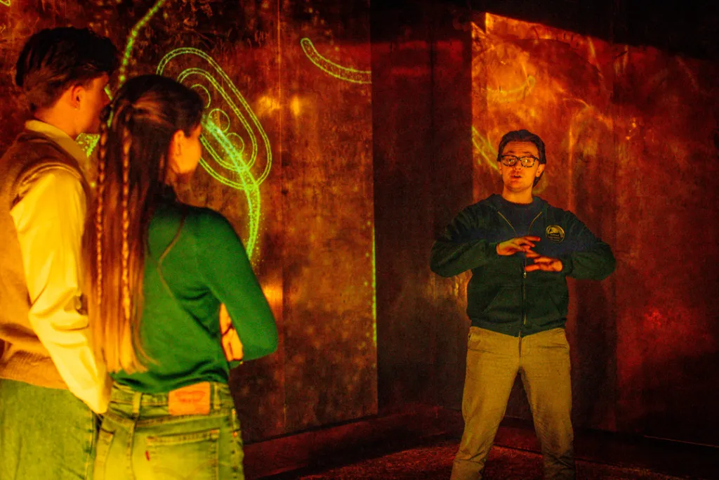 Guide explaining glowing mythic symbols to two visitors during an immersive Irish folklore storytelling moment at the National Leprechaun Museum.