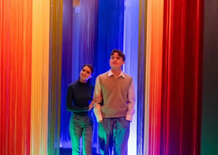 Woman and man walking through a vibrant rainbow tunnel installation at the National Leprechaun Museum, surrounded by colourful hanging strands.