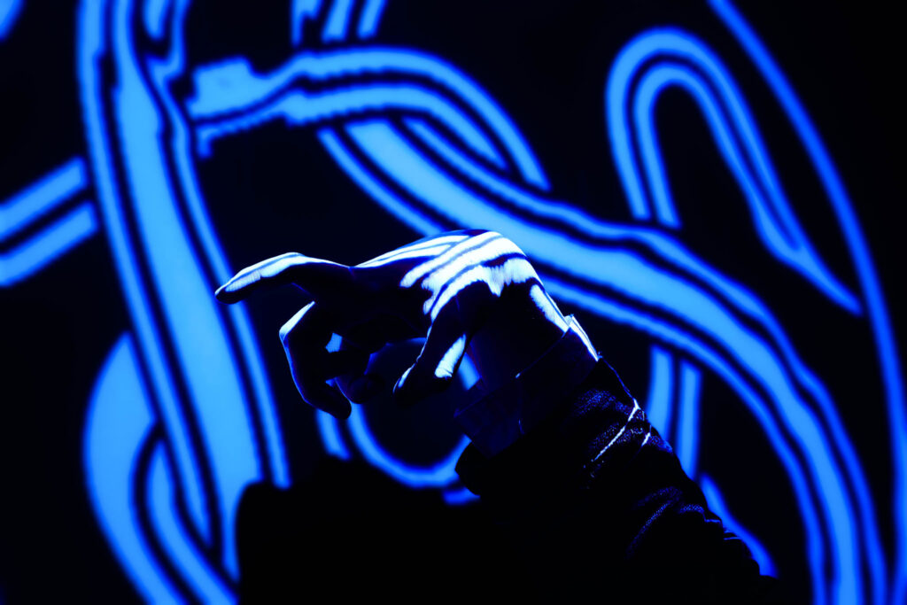 An outstretched hand in a clawed gesture is illuminated by a blue celtic spiral.
