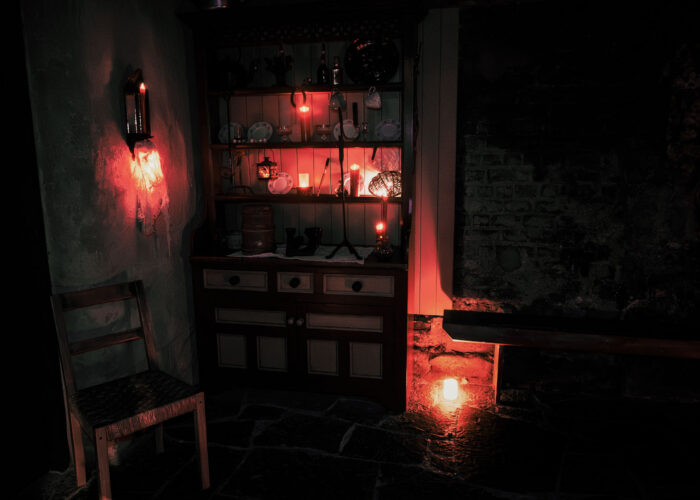 A rustic, Irish style cottage. The scene is dark, illuminated by red glows from candlelight.