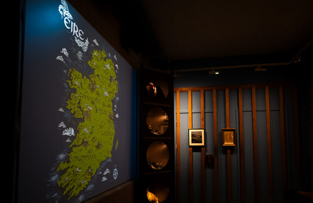 The first room of the museum. There is a large projection of the map of Ireland on one wall. Beside it, a cabinet displaying objects associated with Irish folklore