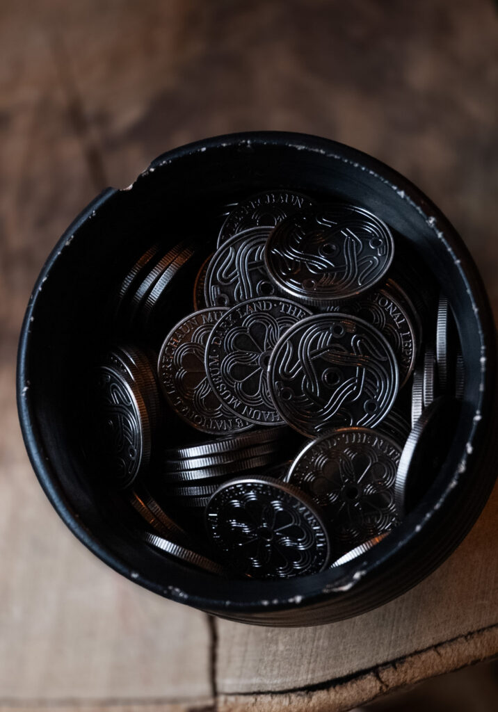 A dark pot filled with silver coins, each emblazoned with the Darkland logo, an interlocking celtic spiral.