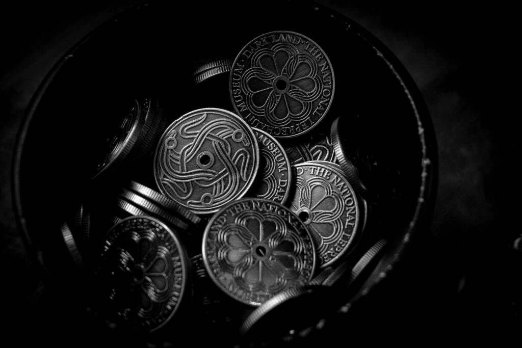 A black and white image of a pot of silver coins. Each coin displays the darkland logo, or a four leafed clover.