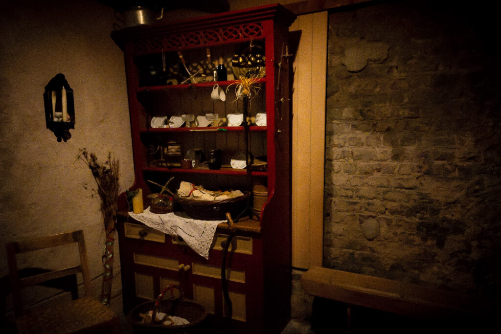 An antique red cabinet in a rustic cottage. Arranged on it are various plates, glasses, candles and wicker baskets.