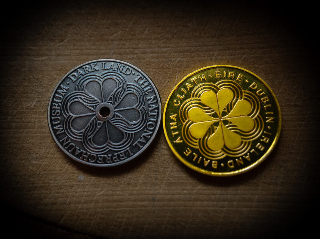 Two coins, side by side, each emblazoned with a four leafed clover logo. One is silver, one is gold.