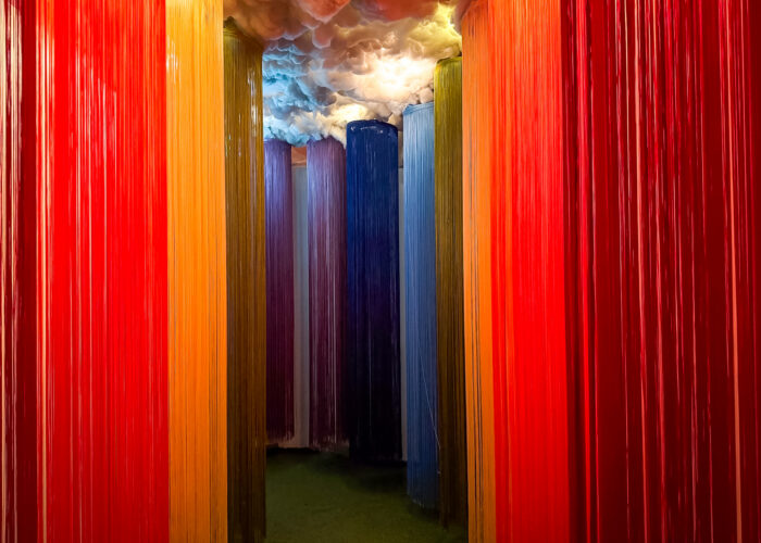 A rainbow-themed corridor, with long strings in the colours of the rainbow hanging from a cloud like ceiling.