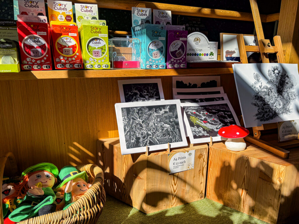 A close up of souvenirs available in the museum gift shop. Story Cubes, mood rings and illustrated prints can be seen on wooden shelves, along with leprechaun plush toys in a small, wicker basket.